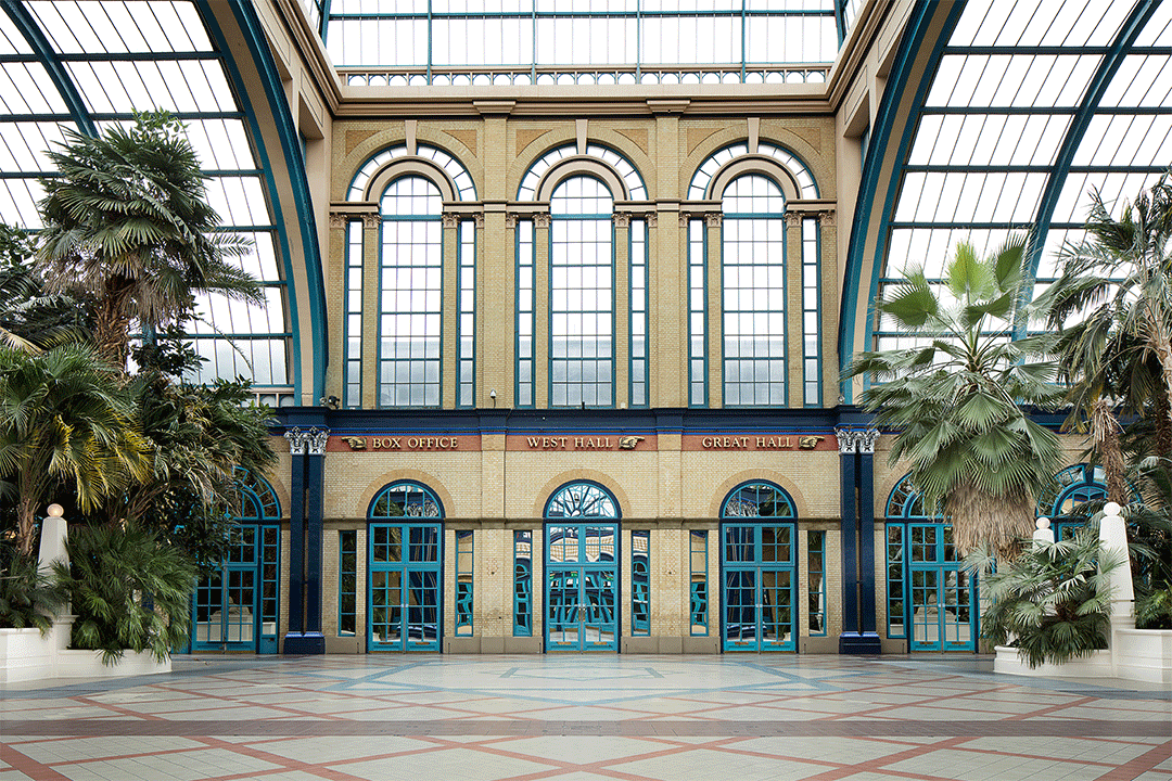 Empty hall with high windows, skylights, and palm trees.
