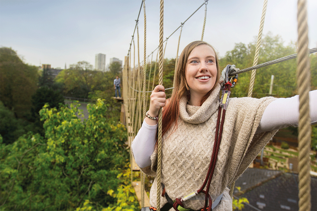 A woman on a rope bridge, smiling at Go Ape at Alexandra Palace.