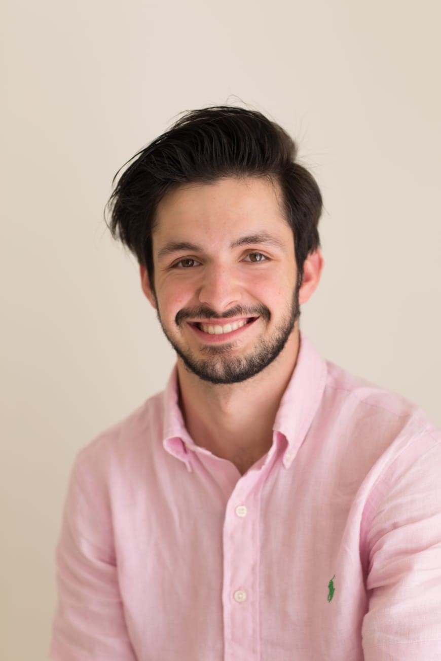 Man with dark hair and pink shirt smiling