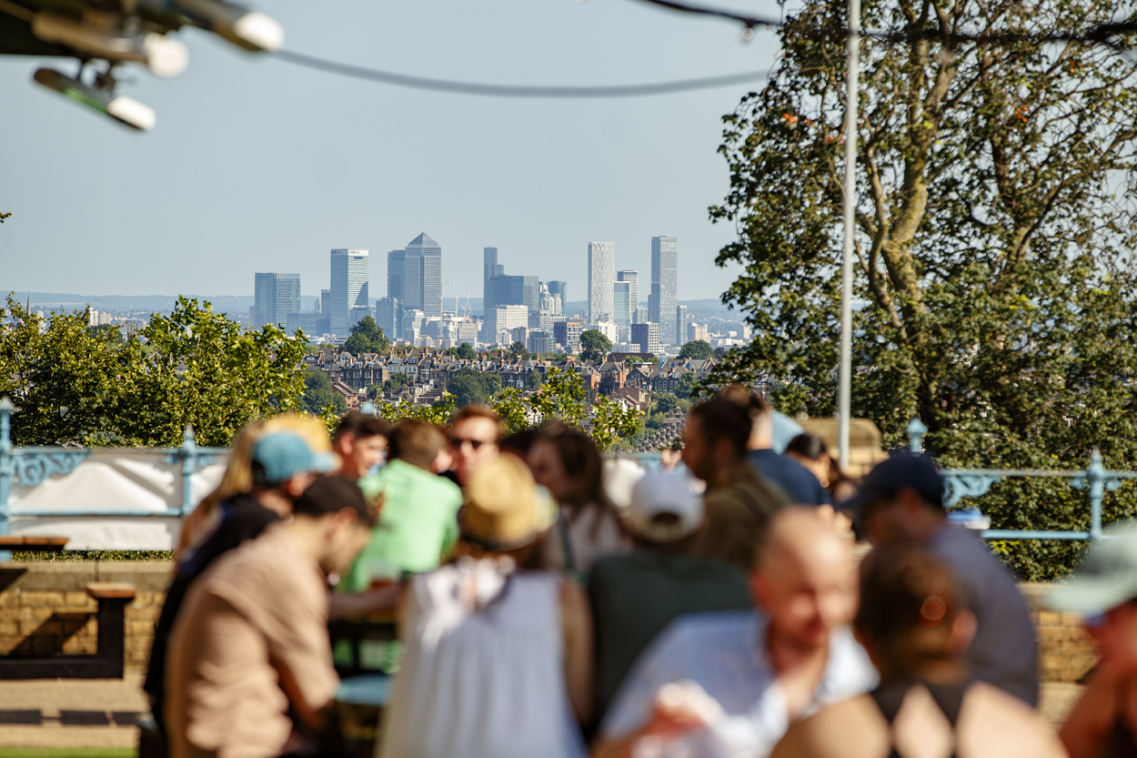 Group of people enjoying a terrace on a sunny day with a view of Canary Wharf.