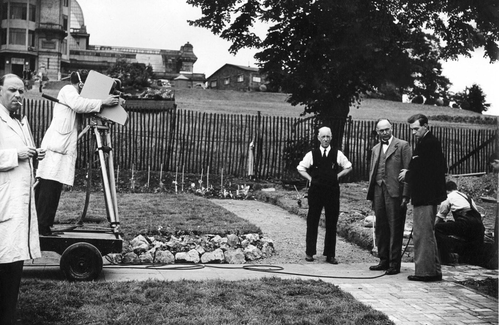 Vintage photograph of three men in a garden being filmed by large television cameras.
