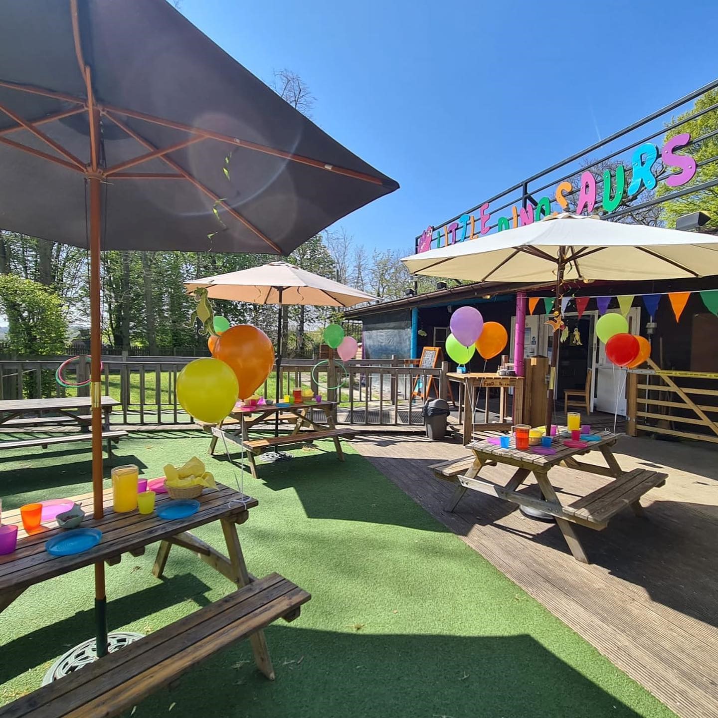 A patio at Little Dinosaurs featuring a table and chairs, adorned with umbrellas and colourful balloons, creating a festive outdoor atmosphere.