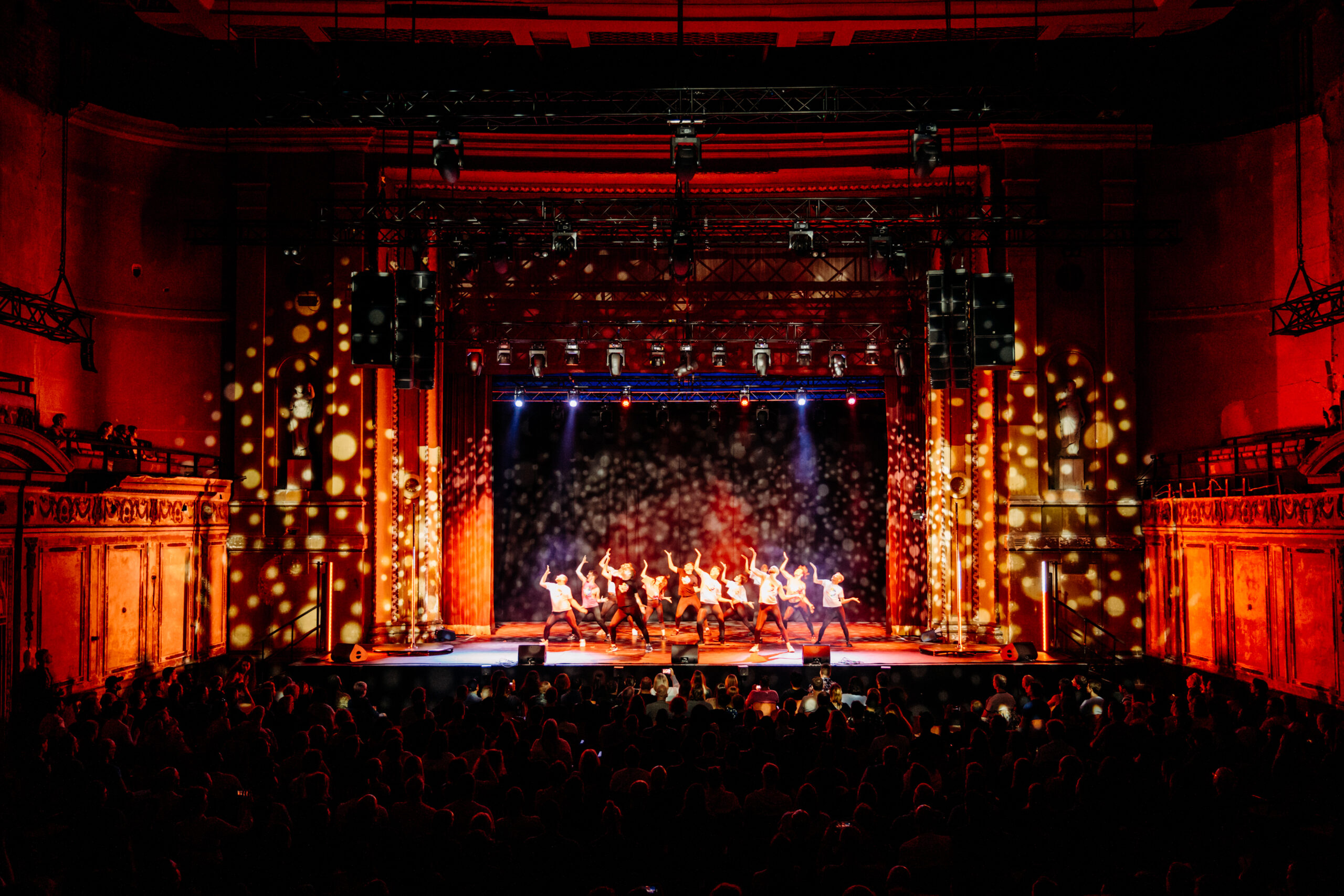 Alexandra Palace stage illuminated by bright lights, featuring a crowd of people engaged in a performance or event.